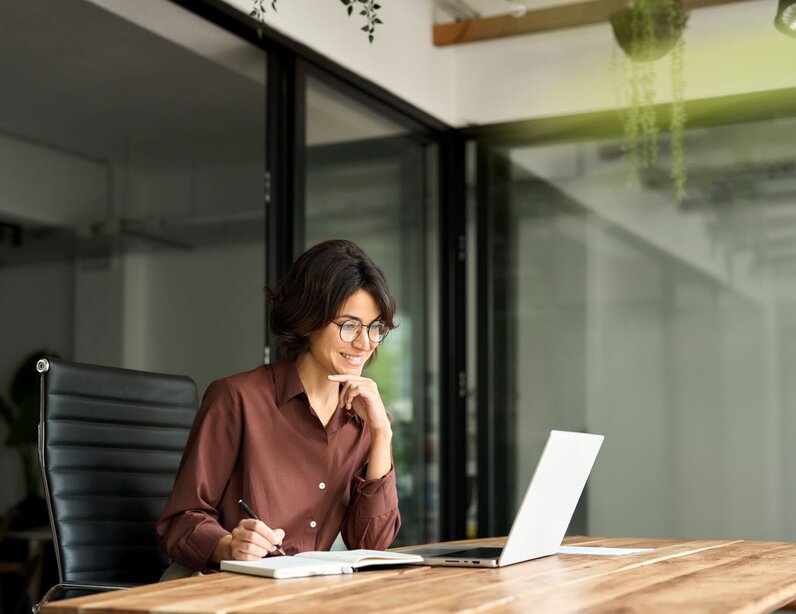 Frau sitzt auf einem Stuhl am Schreibtisch und arbeitet am Laptop