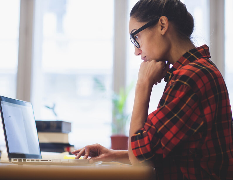 Frau sitzt am Schreibtisch und arbeitet am Laptop