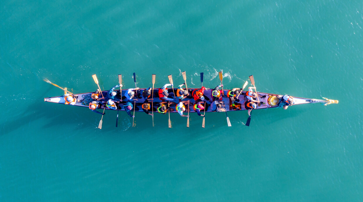 Gruppe sitzt im Ruderboot. Symbolbild für Onboarding